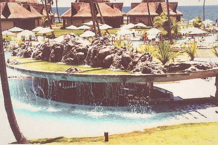Piscina com ilha de pedra diante de bangalôs de palha, à beira-mar, em 2000
