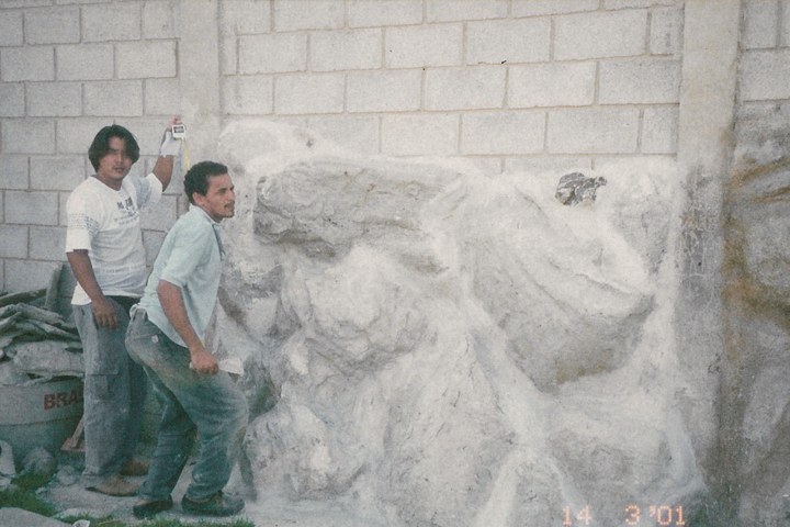 Dois homens dando forma à mão a uma parede de rocha, em 2001