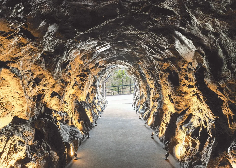 Gruta de rocha moldada, iluminada rente ao chão, no caminho para o elevador do Chalé Cristal